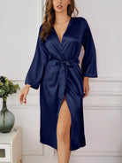 Femme debout portant le peignoir en satin bleu marine Léa, avec une ceinture nouée à la taille, manches longues et tissu fluide au fini brillant, offrant une allure raffinée et un confort luxueux pour les moments de détente à la maison.