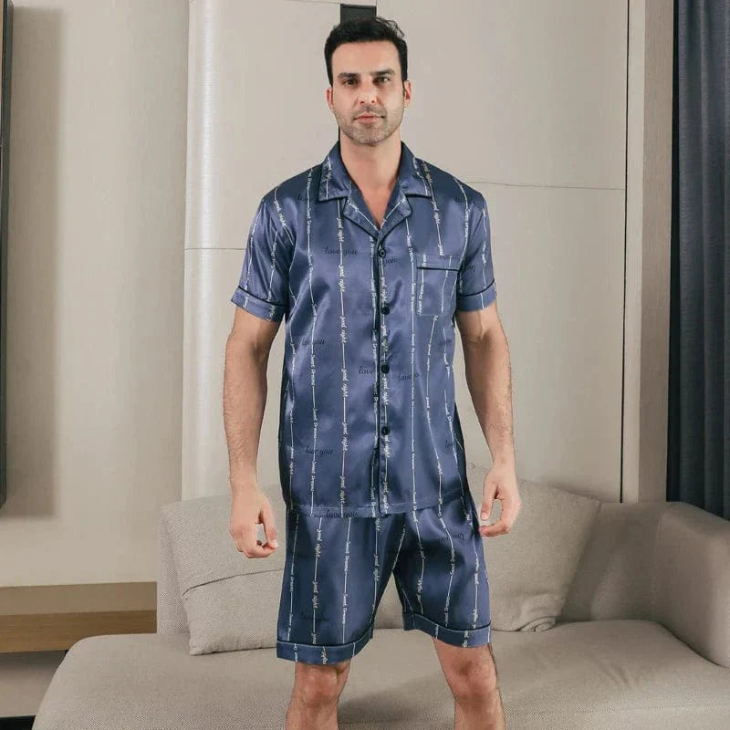 Shorty en satin pour homme, avec une chemise à manches courtes et un short assorti. Le modèle porte le pyjama, affichant une attitude confiante et élégante dans un cadre moderne. Le tissu satiné, doux et léger, offre un confort optimal tout en conservant un style raffiné. Idéal pour les moments de détente à la maison.