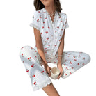 Pyjama femme deux pièces blanc à rayures fines, décoré de motifs cerises rouges, avec manches courtes, dentelle blanche sur le col et les ourlets. Ensemble léger et confortable, parfait pour les matinées détendues à la maison.