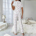 Vue arrière d’un pyjama femme blanc à motifs cerises rouges, composé d’un haut à manches courtes et d’un pantalon long, avec détails en dentelle blanche aux manches et aux chevilles. Ensemble léger, confortable et idéal pour les nuits d'été ou les matins cocooning.