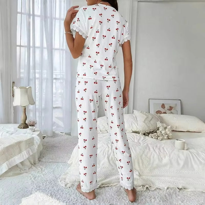 Vue arrière d’un pyjama femme blanc à motifs cerises rouges, composé d’un haut à manches courtes et d’un pantalon long, avec détails en dentelle blanche aux manches et aux chevilles. Ensemble léger, confortable et idéal pour les nuits d&