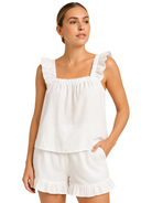 Femme portant un pyjama deux pièces blanc cassé, composé d’un débardeur à larges bretelles volantées et d’un short assorti à volants. Ensemble tendance, léger et agréable à porter, parfait pour les nuits d’été ou les journées détente à la maison.