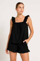 Femme portant un pyjama noir deux pièces, composé d’un débardeur à larges bretelles volantées et d’un short assorti avec volants. Ensemble chic, tendance et confortable, idéal pour les nuits d’été ou les moments de détente à la maison.