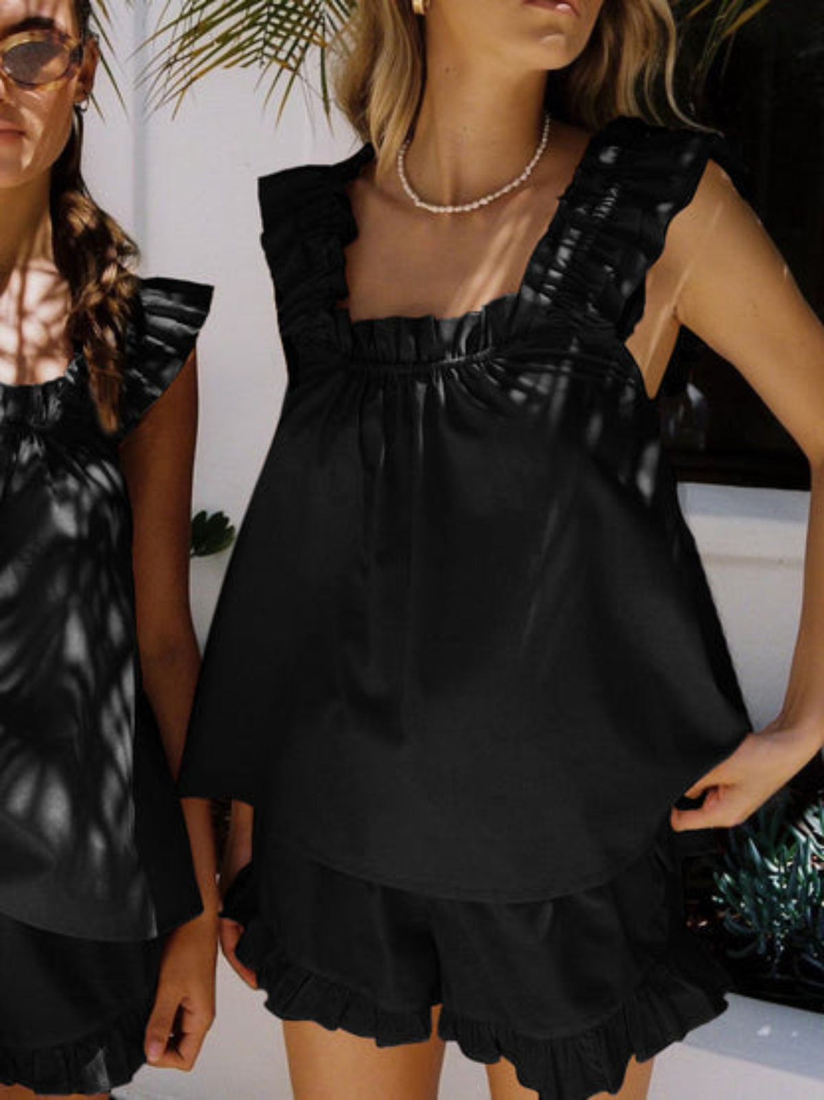 Deux femmes portant le pyjama noir Larkin, composé d’un débardeur à larges bretelles volantées et d’un short assorti avec volants. Ensemble tendance, fluide et agréable, idéal pour les journées d’été ou les moments de détente élégants à l’extérieur.