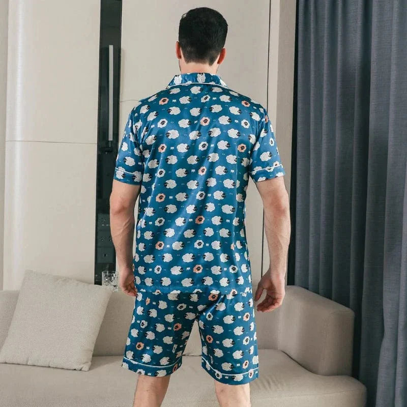 Vue arrière d’un homme portant le pyjama satin Laurent pour homme, ensemble deux pièces avec chemise à manches courtes et short assorti, imprimé bleu à motifs répétés, coupe droite, présenté dans un intérieur moderne.