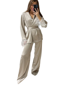 Femme portant un pyjama satiné beige élégant avec des détails en plumes sur les poignets. Le set inclut un haut à col en V avec ceinture à la taille et un pantalon fluide, créant un look raffiné et chic, parfait pour les moments de détente ou une soirée élégante à la maison.
