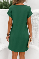 Vue arrière d'une femme portant une robe courte verte à rayures, élégante et légère, parfaite pour l'été. La robe présente un design simple avec des manches retroussées et un tissu fluide, idéale pour un look décontracté et stylé.