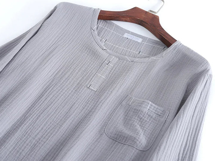 Gros plan sur un haut de pyjama homme en tissu gris clair, avec encolure ronde, petite patte de boutonnage décorative et poche poitrine. Matière douce, légère et confortable, idéale pour un usage quotidien et des nuits paisibles.