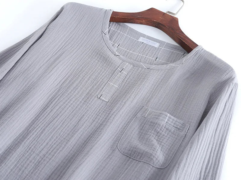 Gros plan sur un haut de pyjama homme en tissu gris clair, avec encolure ronde, petite patte de boutonnage décorative et poche poitrine. Matière douce, légère et confortable, idéale pour un usage quotidien et des nuits paisibles.