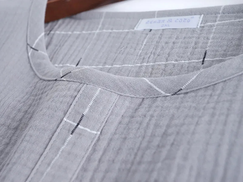 Gros plan sur l’encolure ronde et la patte de boutonnage décorative d’un haut de pyjama homme en tissu gris clair gaufré à fines lignes. Matière douce, respirante et très confortable.