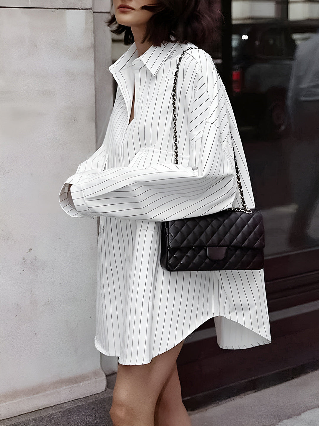 Robe-chemise Lexi pour femme, coupe ample et confortable, coloris blanc à rayures fines, manches longues et col classique, portée avec un sac noir matelassé pour un look tendance et élégant en ville.