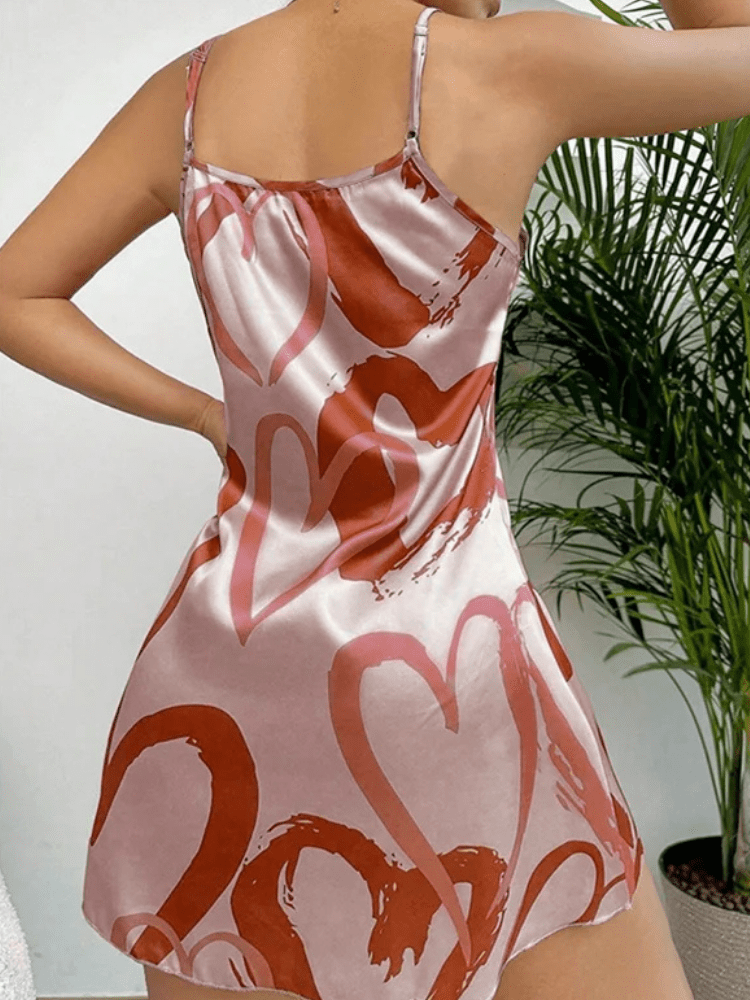 Femme portant la nuisette Lilou en satin rose clair, ornée de cœurs imprimés rose foncé. Coupe courte, fluide et élégante avec fines bretelles réglables. Tissu brillant et doux pour un confort optimal à la maison. Style féminin et raffiné, parfait pour une touche romantique et délicate.