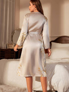 Peignoir femme élégant Linnet en satin ivoire à motif floral doré, coupe midi ceinturée avec manches longues, vue de dos dans une chambre.