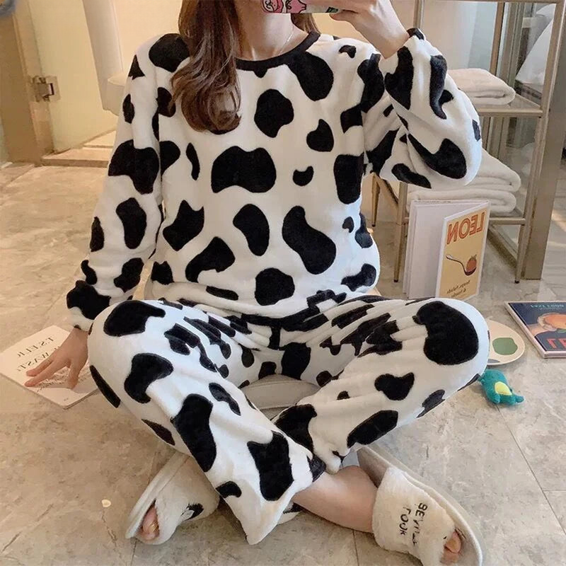 Femme portant un pyjama moelleux imprimé vache, composé d’un haut doux à manches longues et d’un pantalon assorti en tissu blanc à taches noires. Ensemble chaud, confortable et relaxant, idéal pour le cocooning à la maison.