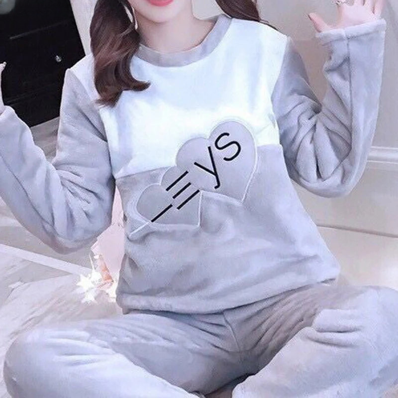 Femme portant un pyjama moelleux gris et blanc avec deux cœurs décoratifs et des lettres sur le haut. Ensemble à manches longues avec pantalon assorti, doux, chaud et relaxant, parfait pour le cocooning à la maison.