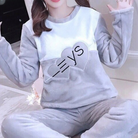 Femme portant un pyjama moelleux gris et blanc avec deux cœurs décoratifs et des lettres sur le haut. Ensemble à manches longues avec pantalon assorti, doux, chaud et relaxant, parfait pour le cocooning à la maison.