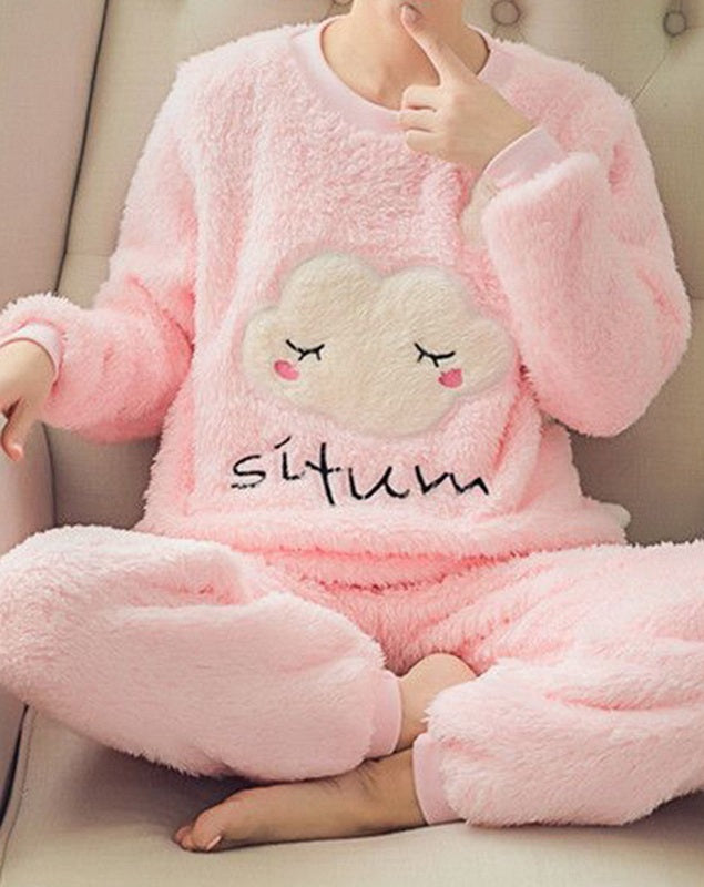 Femme portant un pyjama moelleux rose composé d’un haut doux à manches longues décoré d’un nuage endormi brodé et d’un pantalon assorti. Ensemble confortable, chaleureux et relaxant, idéal pour le cocooning à la maison.