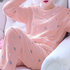 Femme portant un pyjama moelleux rose pastel décoré de petits pois colorés, composé d’un haut doux à manches longues et d’un pantalon assorti. Ensemble confortable, chaud et relaxant, idéal pour le cocooning à la maison.