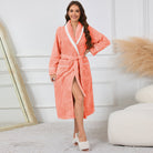 Peignoir femme confortable Lison en tissu gaufré corail avec col châle blanc, ceinture et poches, porté debout en intérieur.