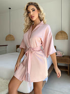 Cardigan pyjama femme Livie en satin rose poudré, coupe courte avec manches amples et ceinture à nouer, porté debout dans une chambre lumineuse.