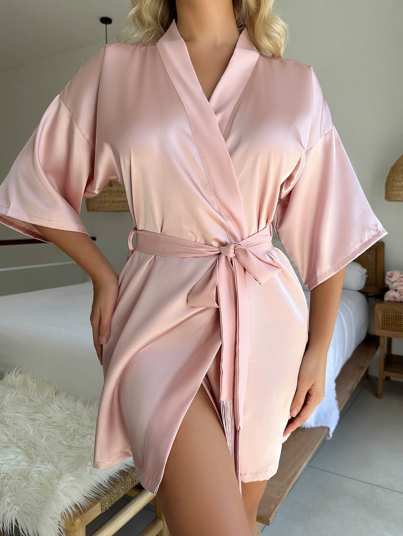 Gros plan du cardigan pyjama femme Livie en satin rose poudré, ceinture à nouer à la taille et manches amples, porté en intérieur.