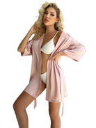 Cardigan pyjama femme Livie  en satin rose poudré, coupe courte avec manches 3/4 et ceinture à nouer, porté ouvert sur lingerie blanche dans une chambre.