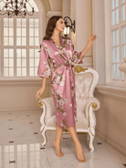 un peignoir long en satin rose à motifs floraux, doté d’une ceinture, offrant une allure raffinée et luxueuse.