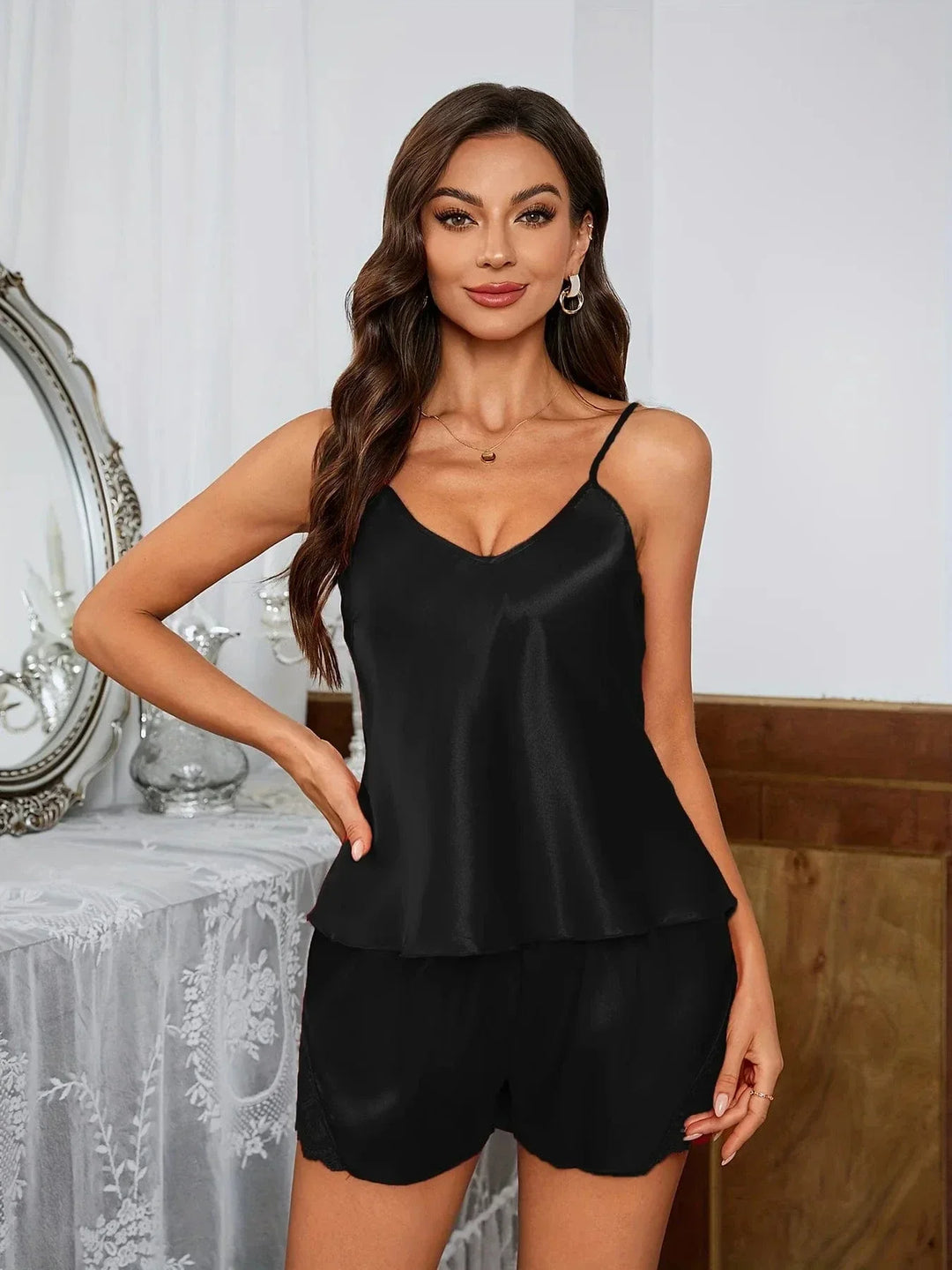 Femme portant un pyjama deux pièces en satin noir, composé d’un débardeur à fines bretelles et d’un short fluide avec finitions discrètes en dentelle. Ensemble léger, confortable et élégant, parfait pour les nuits douces et les moments de détente avec style.