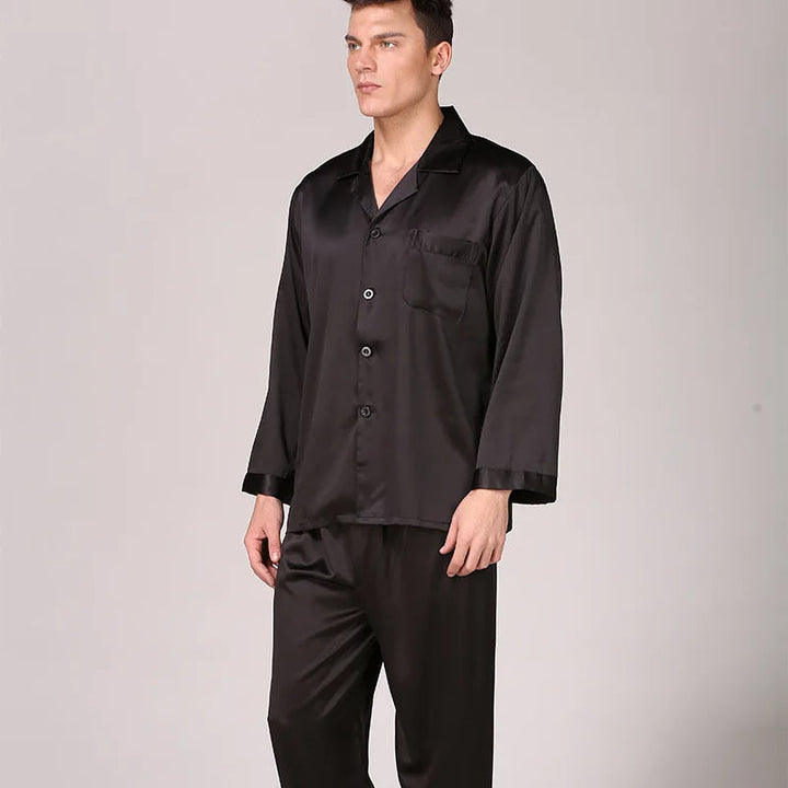 Homme portant un pyjama satiné bleu marine composé d’une chemise à manches longues avec poche poitrine et d’un pantalon assorti. Ensemble doux, élégant et très confortable, idéal pour des nuits sophistiquées et agréables.