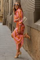 Robe à rayures roses et orange, de style portefeuille, avec des manches longues et une coupe fluide, parfaite pour un look chic et décontracté.
