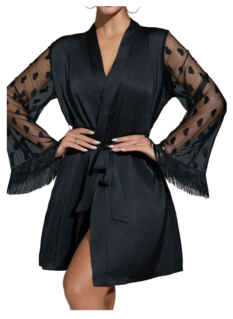 Femme portant le peignoir Lucie noir satiné, avec manches longues en tulle transparent ornées de motifs cœurs et finitions à franges. Ceinture à nouer à la taille. Modèle élégant et séduisant, idéal pour une allure glamour à la maison.