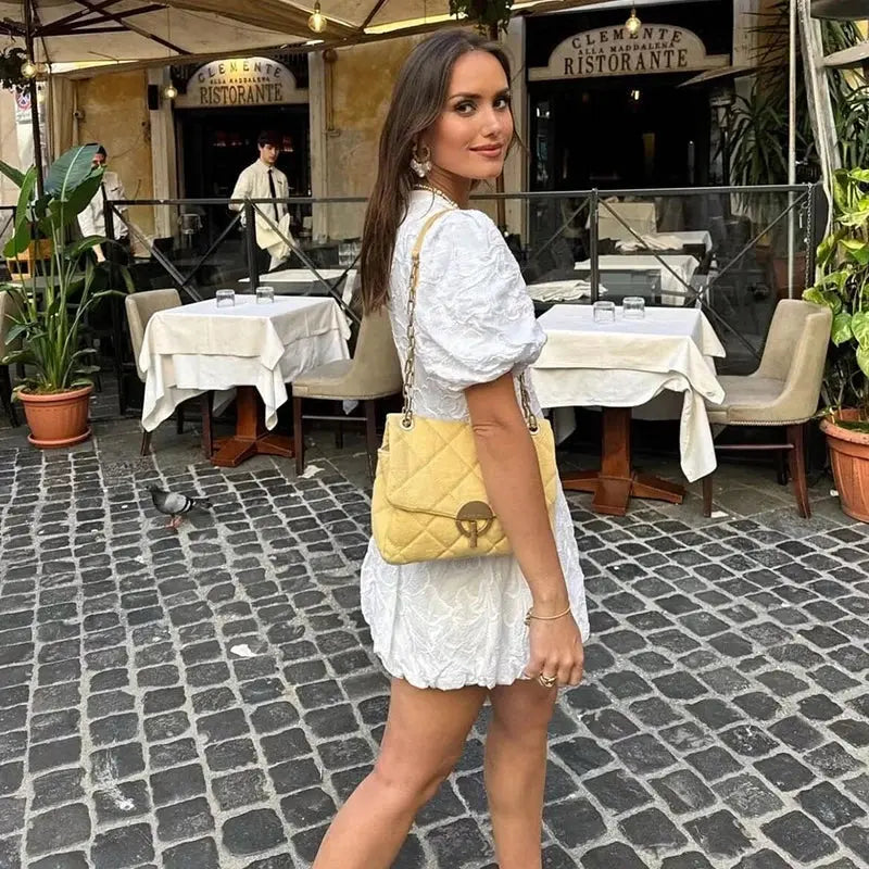 Robe mini satin blanche Lydie vue de dos portée en terrasse, coupe courte et fluide avec manches bouffantes, look élégant et féminin idéal pour l’été.