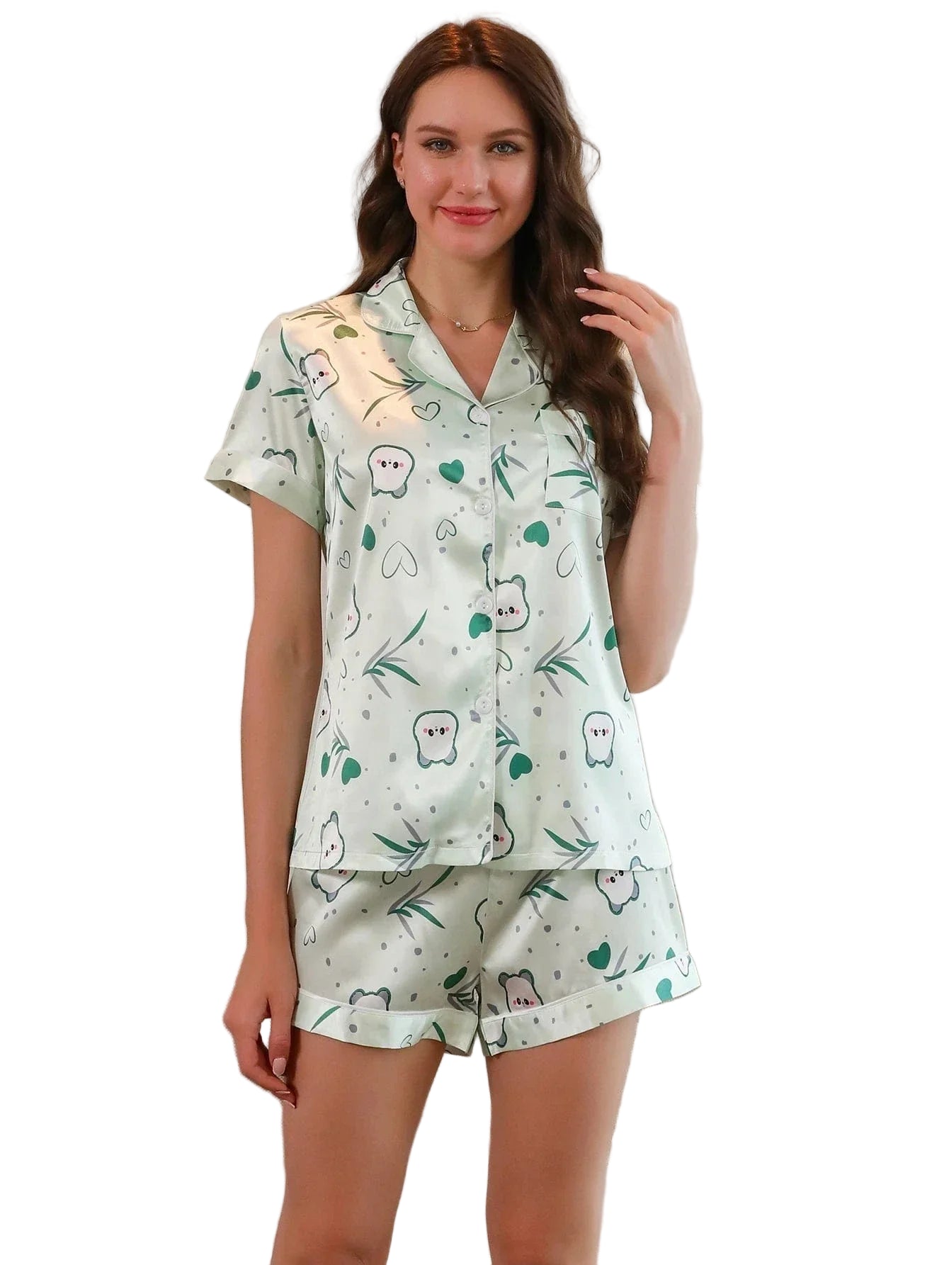 Femme portant un pyjama court en satin imprimé, composé d’un haut à manches courtes boutonné et d’un short assorti. Motifs mignons de petits personnages, cœurs et feuillages verts sur fond clair. Ensemble léger, doux et agréable, parfait pour les nuits d’été ou les moments de détente à la maison.