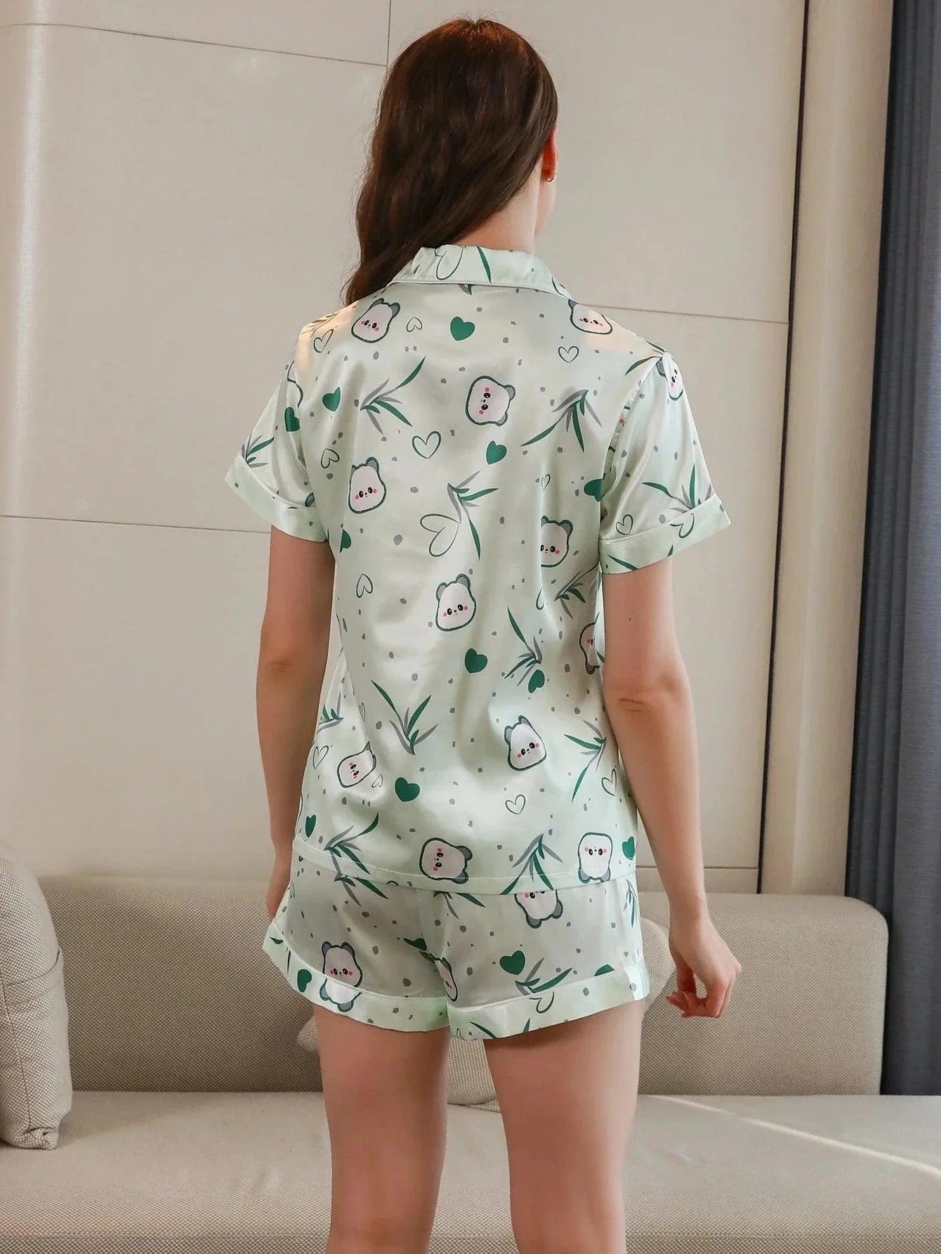 Vue de dos d’une femme portant un pyjama court en satin, composé d’un haut à manches courtes et d’un short assorti, avec imprimés adorables de petits personnages, cœurs et feuillage vert. Ensemble léger, confortable et agréable pour les nuits d'été ou les moments de détente à la maison.