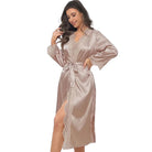 Femme portant le peignoir Mélodie en satin beige rosé, orné de dentelle délicate au col, aux manches et le long de la fermeture. Ce modèle mi-long, ceinturé à la taille, offre une allure élégante et raffinée tout en assurant un confort optimal. Idéal pour les moments de détente à la maison.