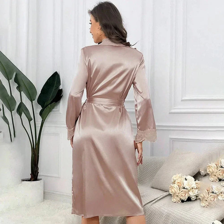 Vue de dos du peignoir Mélodie en satin femme, couleur champagne, avec ceinture à nouer et manches longues bordées de dentelle. Tissu fluide et brillant offrant un tombé élégant. Ambiance cosy et raffinée avec décor floral et mobilier doux. Un vêtement confortable pour les moments de détente à la maison.