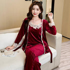 Femme assise sur un canapé portant un pyjama en velours bordeaux avec dentelle blanche, composé d’un débardeur, d’un pantalon long et d’un peignoir assorti. Ensemble élégant, raffiné et confortable, idéal pour les soirées cocooning avec style.