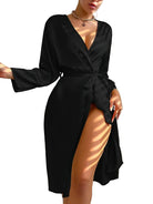 Femme portant un peignoir noir satiné, coupe croisée avec ceinture à nouer à la taille et manches longues. Modèle fluide, léger et élégant, parfait pour un moment de détente chic ou une touche sensuelle à la maison.