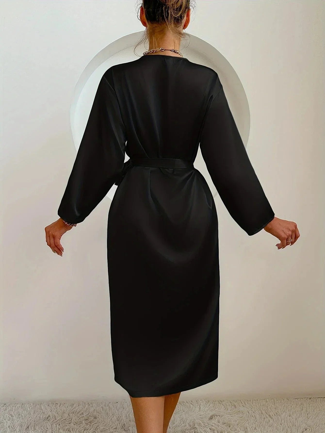 Vue de dos d'une femme portant un peignoir noir satiné à manches longues, ceinturé à la taille. Modèle fluide, élégant et confortable, idéal pour les moments de détente à la maison avec une touche de raffinement.