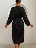 Vue de dos d'une femme portant un peignoir noir satiné à manches longues, ceinturé à la taille. Modèle fluide, élégant et confortable, idéal pour les moments de détente à la maison avec une touche de raffinement.