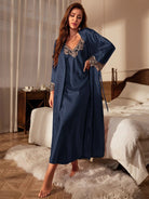 Femme debout dans une chambre élégante, vêtue d’une nuisette longue satinée bleu nuit avec détails en dentelle beige sur le col et les poignets, accompagnée d’un peignoir assorti. Ensemble de nuit chic, doux et raffiné, parfait pour allier confort et féminité.