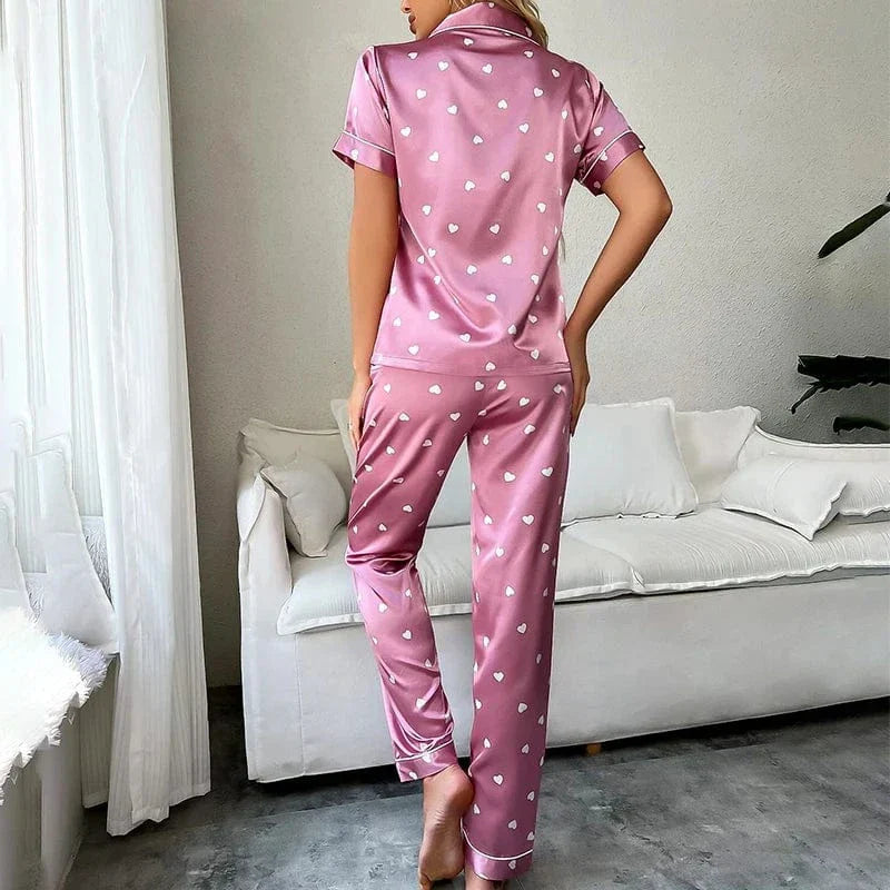Vue arrière d’une femme portant le pyjama Pyjama femme Doux, élégant & agréable , un ensemble satiné rose décoré de petits cœurs blancs, composé d’une chemise à manches courtes et d’un pantalon fluide, idéal pour des nuits douces et confortables.