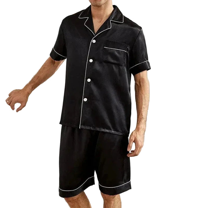 Homme debout portant le pyjama satin pour homme Marcel, ensemble élégant et confortable composé d’une chemise à manches courtes boutonnée et d’un short assorti, en satin noir avec liserés contrastés, offrant une allure raffinée et un confort idéal pour la nuit ou la détente à la maison.