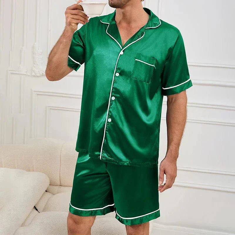Homme debout tenant une tasse, portant le pyjama satin pour homme Marcel, ensemble élégant et confortable composé d’une chemise à manches courtes boutonnée et d’un short assorti, en satin vert avec liserés contrastés, offrant une allure raffinée et un confort idéal pour la détente à la maison ou la nuit.