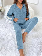 Femme assise confortablement sur un tapis blanc moelleux, portant un pyjama deux pièces bleu ciel en tissu pelucheux avec fermeture éclair et bandes blanches sur les manches et les jambes, alliant style décontracté et chaleur douillette.