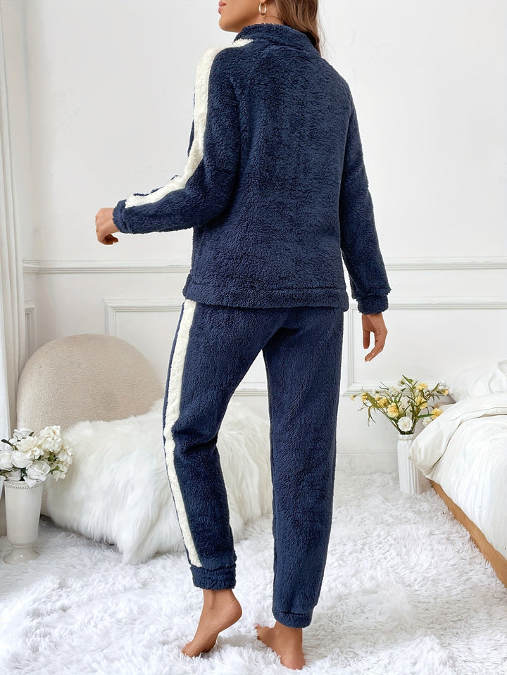 Vue arrière d’une femme portant un pyjama femme deux pièces en tissu pelucheux bleu marine avec bandes contrastantes blanches sur les manches et les jambes, dans une chambre cosy décorée de fleurs, parfaite pour les moments de détente à la maison.