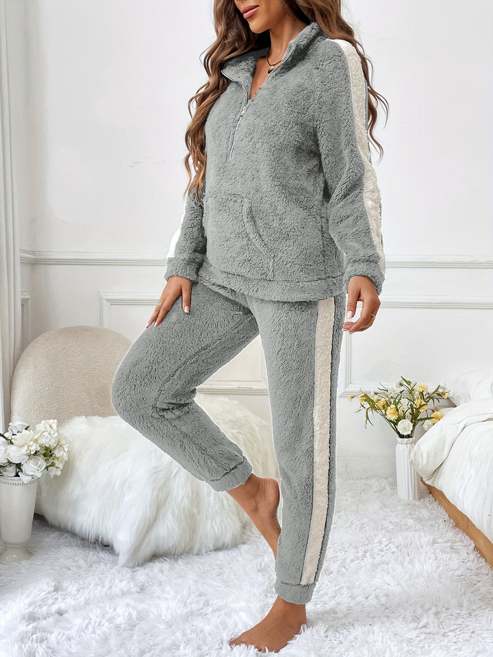Femme portant un pyjama deux pièces gris clair en matière douce et moelleuse, avec des bandes blanches contrastantes sur les manches et les jambes, posant dans une chambre douillette à la décoration élégante et lumineuse.