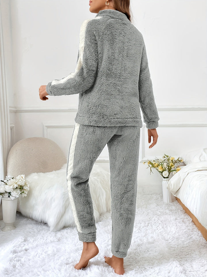 Femme de dos portant un pyjama gris clair deux pièces en tissu pelucheux, avec bandes blanches sur les bras et les jambes, dans une chambre élégante à la décoration cosy avec un lit douillet et un tapis en fausse fourrure.