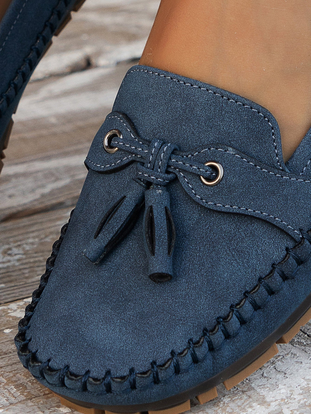 Gros plan sur les mocassins bleus, mettant en valeur les détails raffinés. On aperçoit le nœud décoratif en cuir et les coutures soignées qui ajoutent une touche élégante. Les œillets en métal et le cuir doux soulignent le confort et le style de ces mocassins parfaits pour une allure décontractée et chic.