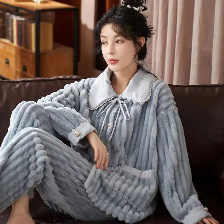 Femme portant un pyjama en flanelle bleu-gris, chaud, doux et très élégant, avec col large décoré de perles, manches longues et pantalon assorti à texture en relief. Tenue cocooning idéale pour un confort maximal à la maison.